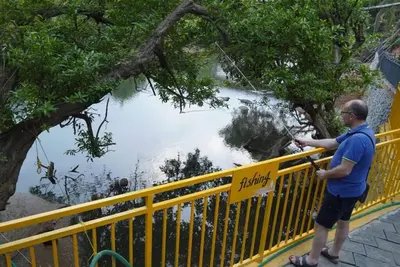 a man standing on a yellow fence looking at a river at Mazhavilkadu ForestResort & Restaurant in Kozhikode