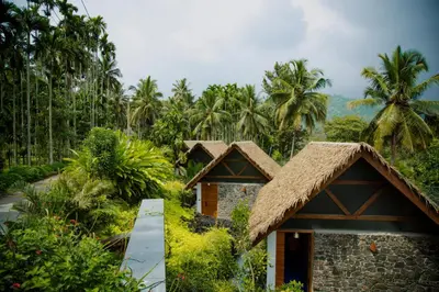 a cottage in the jungle with palm trees in the background at Maayaa riverside villa by KPM Tripenta in Attappādi