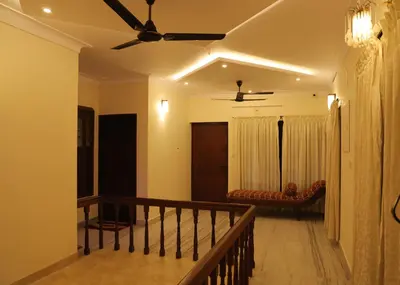 a living room with a ceiling fan and a staircase at Malpans Mansion in Nedumbassery