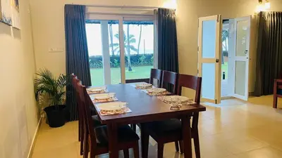 a dining room table with chairs and a table with plates and dishes at Seagrove Villa in Kappad
