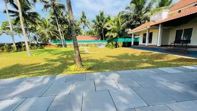 a patio in front of a house with palm trees at Seagrove Villa in Kappad