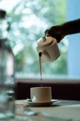 a person pouring coffee into a cup on a table at Lilac Hotel Guruvayur in Guruvāyūr