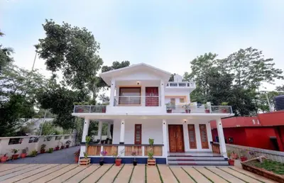 a large white house with a balcony on a deck at Greenfield Homestay in Vythiri