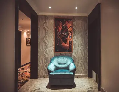 a blue chair in a hallway with a painting at Hotel Golden Riviera in Mysore