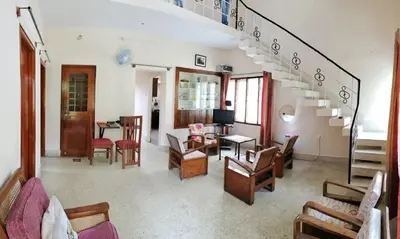 a living room with a staircase with chairs and tables at Raintree Garden in Mysore