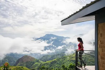 a woman standing on a balcony looking out at the mountains at Zostel Plus Poombarai, Kodaikanal in Kodaikānāl