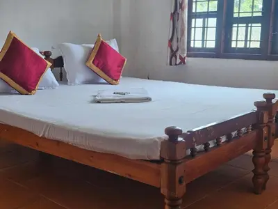 a wooden bed with white sheets and red pillows at Cicily Cottage in Munnar