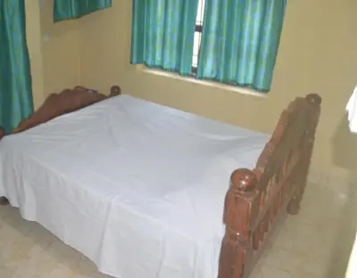 a bedroom with a bed with white sheets and blue curtains at Kalpavruksha Farmstay by StayApart in Madikeri