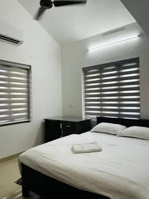 a bedroom with a large white bed with two windows at Saaketh Holiday Home(2) in Kozhikode