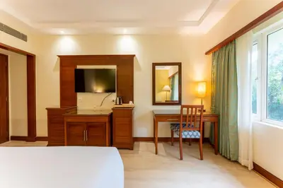a bedroom with a bed and a desk and a mirror at Club Mahindra Golden Landmark, Mysuru in Mysore