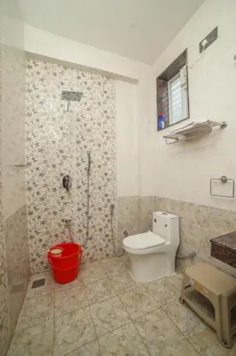 a bathroom with a toilet and a red bucket at AVJ Nest, Kodaikanal in Kodaikānāl