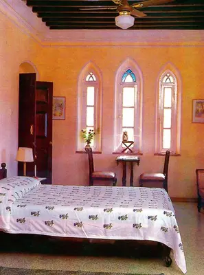 a bedroom with a bed and two chairs and windows at The Green Hotel in Mysore