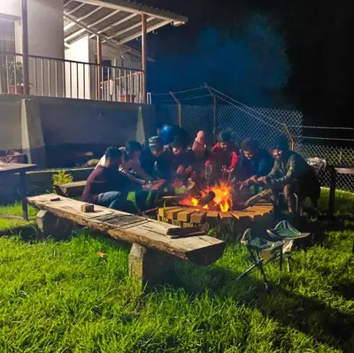 a group of people sitting around a fire at Cloud & Mist Inn-Stay with Mountain Views in Kotagiri, Near Ooty in Kotagiri