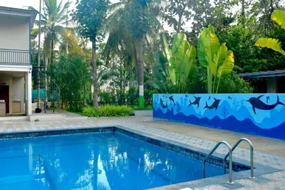 a swimming pool in a yard with a blue wall and trees at Gandhada Goodu Retreat in Kanakapura