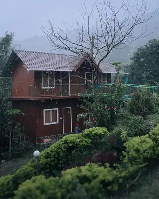 a red house with a balcony and a yard at Don's River Valley Jungle Resort in Marayoor