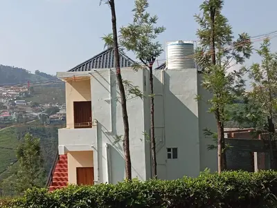 a white house on top of a hill with trees at Sandy Castle Villa 3 Bhk Homestay in Ooty