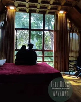 a couple sitting on a bed looking out a window at Tree House Wayanad in Muthanga