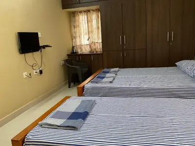 a room with two beds and a tv on the wall at Shantham Service Apartments, Indumanagar, Coimbatore in Coimbatore