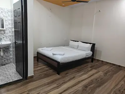 a bedroom with a bed with white sheets and a sink at Comfort Cove Apartments in Mysore