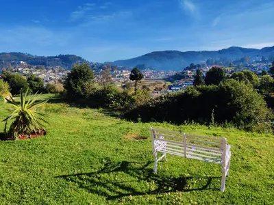 a white bench sitting on top of a green field at Welbeck Vintage By Oxygen Resorts in Ooty