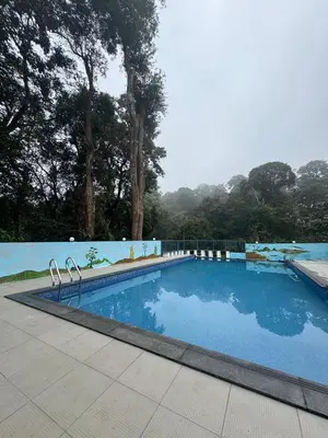 a swimming pool with blue water and trees in the background at Wayanad Palace in Ambalavayal