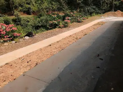 an empty sidewalk next to a garden with flowers at Creek Side in Madikeri