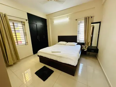 a bedroom with a bed and two windows at Oryx Hotel Apartments in Mysore