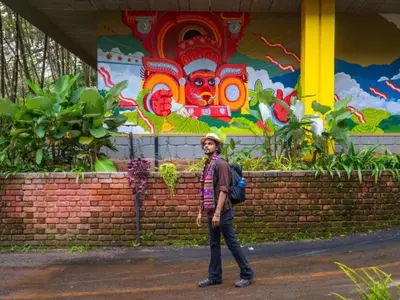 a man standing in front of a wall with a mural at The Hosteller Wayanad, Vythiri in Vythiri