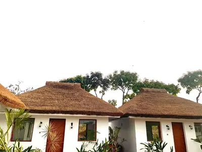 two houses with thatched roofs with trees in the background at CSR Landmark Resorts in Coimbatore