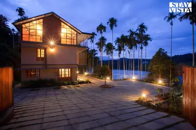 a house with palm trees and lights at night at Rivera The Lake View with Indoor Games by StayVista in Wayanad