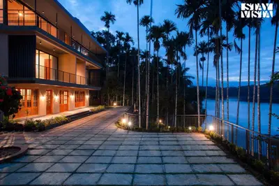 a building with a walkway next to a body of water at Rivera The Lake View with Indoor Games by StayVista in Wayanad