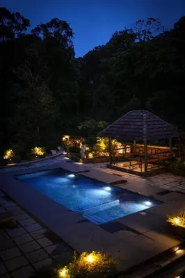 a swimming pool at night with a table and an umbrella at Elixir Woods Luxury Resort And Spa, Munnar in Munnar