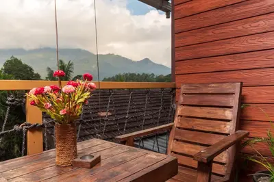 a vase of flowers on a wooden table with a chair at treevillawayanad in Vythiri