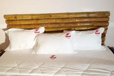 a bed with white pillows and a wooden headboard at The Alpine Inn in Gūdalūr