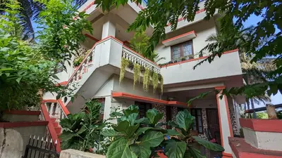 a white building with a balcony and trees at Delight Homestays Coorg in Kushālnagar