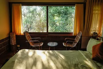 a bedroom with a bed and two chairs and a window at Neelambari Ecotoursm in Trichūr