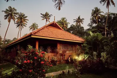 a small house with palm trees in the background at Neelambari Ecotoursm in Trichūr