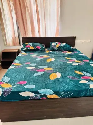 a bed with a green comforter with colorful flowers on it at Soorya Madhavam Apartment Guruvayur - 200 m from temple walkable in Guruvāyūr