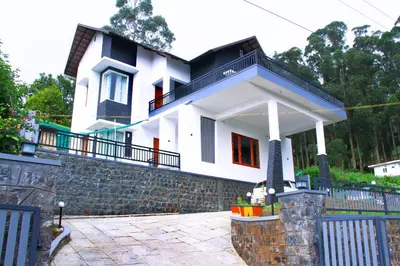 a white house with a balcony on a stone wall at Airy Homestay Ooty by Lexstays in Ooty