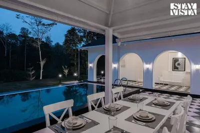 a dining area with a table and chairs next to a swimming pool at Stayvista at Mudra Manor 4BR - Coffee Estate Comp Breakfast Big Heated Pool in Madikeri