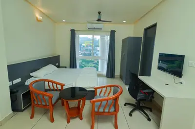 a bedroom with a table and two chairs and a desk at RIVULET HOTEL APARTMENTS in Mukkam