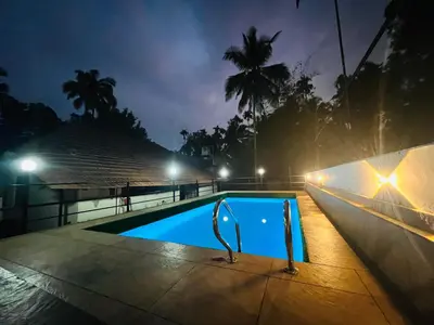 a swimming pool at night with palm trees at Paroommel Haven Wayanad in Kenichira