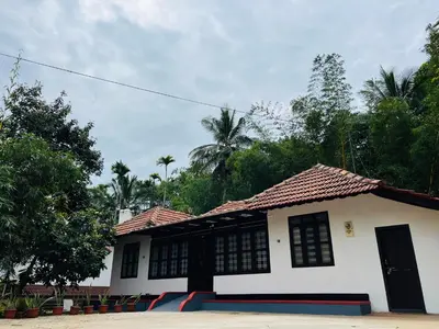 a white house with a black door and trees at Paroommel Haven Wayanad in Kenichira