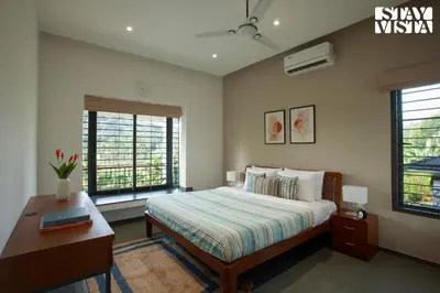 a bedroom with a bed and a desk and two windows at StayVista at The Big Chill with Breakfast Included in Wayanad