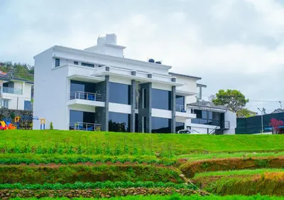a white house on top of a green hill at Kodai Outdoor Valley in Kodaikānāl