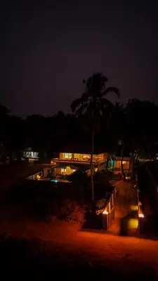 a building with a palm tree and a pool at night at Kappad Beach House by Kisah Stays in Kappad