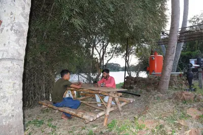 two men sitting at a picnic table under a tree at Golden Triangle River side Cabin in Mysore
