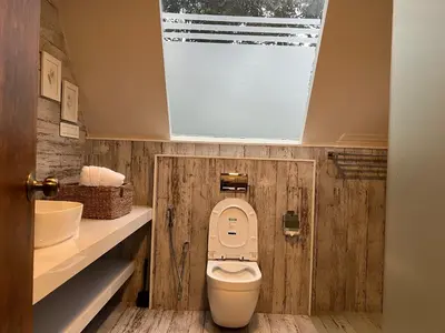 a bathroom with a toilet with a window above it at Inika in Ponnampet