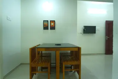 a table with chairs in a room with a white wall at Greens in Kozhikode