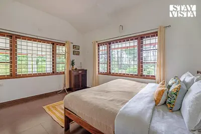 a bedroom with a large bed and two windows at StayVista at Wellbeing Villa in Wayanad